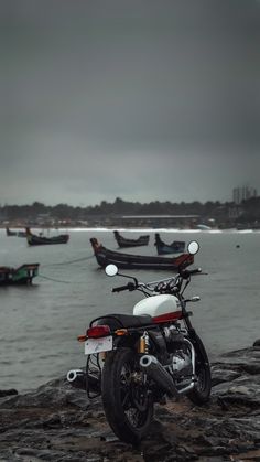 a motorcycle is parked on the rocks by the water and boats are in the background