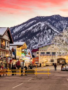 a town with mountains in the background and people walking on the street at night time