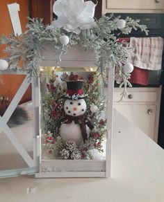 a snowman decoration in a white box on a counter with flowers and greenery