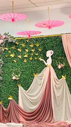 a green wall with pink umbrellas hanging from it's sides and flowers on the floor