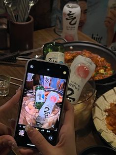 a person holding up a cell phone to take a picture of food on the table