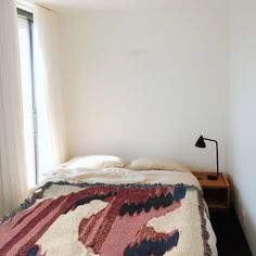 a bed with a colorful blanket on top of it next to a night stand and window