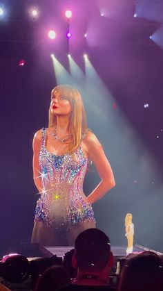 a woman is performing on stage in front of a large group of people and lights