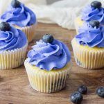 blueberry cupcakes with frosting and blueberries on a wooden cutting board