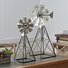 two metal windmills sitting on top of a wooden table next to a vase with flowers