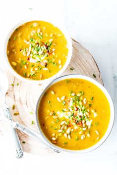 two white bowls filled with soup on top of a wooden plate