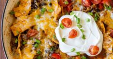 a casserole dish with cheese, black beans, tomatoes and sour cream on top