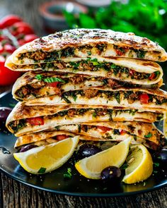 a stack of quesadillas on a plate with lemons and olives