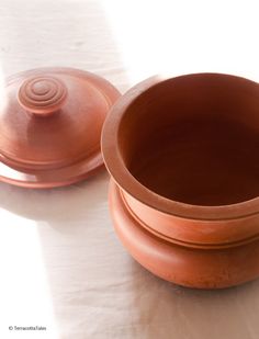 two clay bowls sitting on top of a white table cloth next to a brown lid