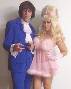 two people dressed in costumes standing next to each other, one is wearing a pink dress and the other wears a blue suit