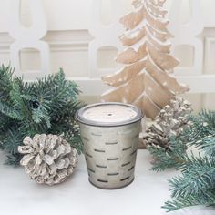 a candle sitting on top of a white table next to pine cones and evergreen branches