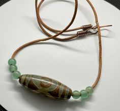 This one-of-a-kind necklace showcases the earthy beauty of Tibet Agate and Green Aventurine, strung on a durable leather cord for a rustic, organic look. The warm copper clasp adds a charming touch to the natural stone pairing, creating a harmonious blend of textures and tones. Perfect for those who appreciate unique, handcrafted jewelry with a bohemian flair. Tibetan Dzi agate is a stone of spiritual healing, courage, strength, clarity, and cleansing. Approximately 20" long.The Copper Component Spiritual Copper Necklace With Natural Stones, Brown Agate Necklace For Meditation, Earthy Hand-strung Agate Necklace, Earthy Beauty, Bohemian Hand-strung Agate Crystal Necklaces, Brown Agate Hand-strung Necklaces, Unique Handcrafted Jewelry, Textures And Tones, Copper Necklace