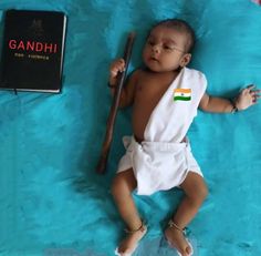 a baby laying on top of a blue blanket next to a book and a bat