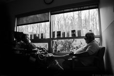 black and white photograph of two people sitting in chairs looking out the window at trees