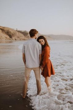 a man and woman standing in the water at the beach looking into the distance with their arms around each other