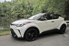 a white toyota c - hr is parked on the side of the road near some trees