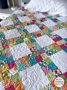 a quilted bed with white sheets and multicolored squares on the bedspread