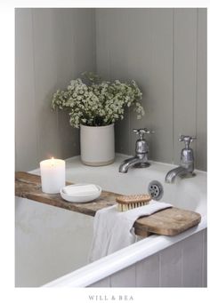 a white bath tub sitting next to a wooden shelf with a candle and soap dispenser