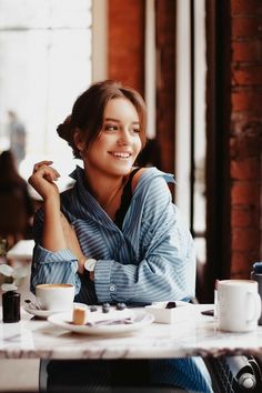 a woman sitting at a table with her arms crossed and coffee cups in front of her