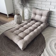 a bed sitting on top of a rug in front of a white brick wall next to a vase