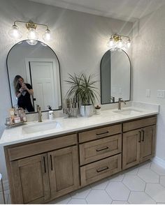 a woman taking a photo of her bathroom vanity with two mirrors and lights above it