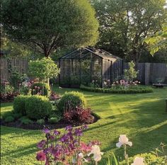 a garden with lots of flowers in it and a small greenhouse behind the fenced off area