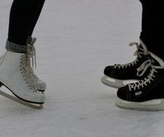 two people in black and white ice skates on the snow with their feet up