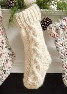 two knitted stockings hanging from a mantel with pine cones on the top and bottom