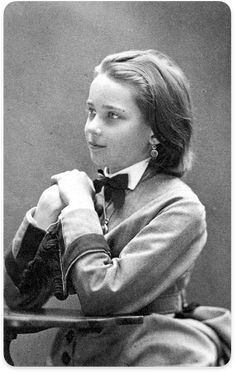 an old black and white photo of a young woman wearing a bow tie, sitting at a table