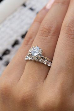 a woman's hand with a diamond ring on top of her finger and the other hand holding an engagement ring