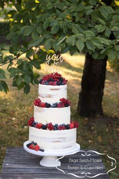 a wedding cake with berries and blueberries sits on a table in front of a tree