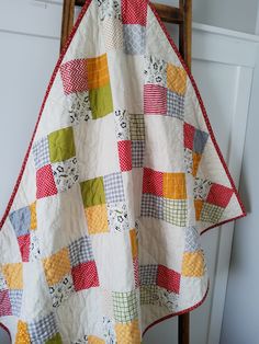 a quilt is hanging on a chair in front of a white wall and wooden ladder