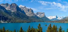 the mountains are covered in snow and blue water, with pine trees on either side