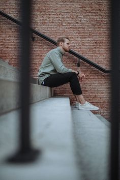 a man sitting on the edge of a set of stairs with his hand in his pocket