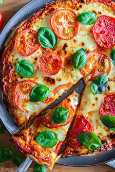 a pizza with cheese, tomatoes and basil leaves on it is cut into slices by a knife