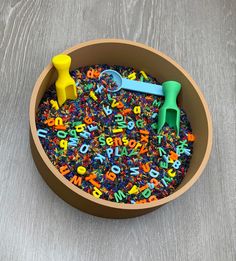 a bowl filled with letters and toys on top of a wooden table next to a pair of scissors