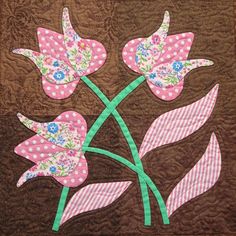 a quilted wall hanging with pink flowers and green stems on it's side