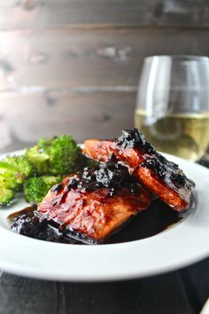 a white plate topped with meat and broccoli next to a glass of wine