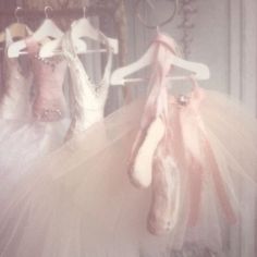 three ballerinas are lined up in tutues and one is hanging on a rack