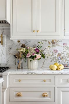 a kitchen with white cabinets and flowers in a vase on the counter top next to an oven