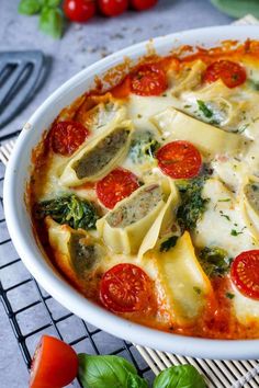 a white dish filled with ravioli, tomatoes and spinach on top of a cooling rack