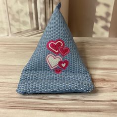 a blue triangle shaped pillow with hearts on the front and back, sitting on a wooden table