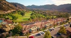 an aerial view of a golf course surrounded by mountains and houses with cars parked in the lot