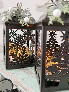 two black lanterns decorated with christmas trees and snowflakes are sitting on a table