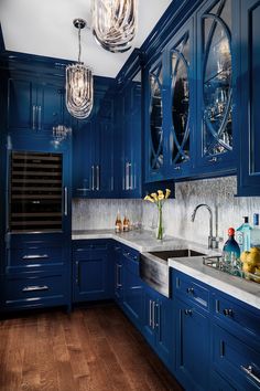 a kitchen with blue cabinets and marble counter tops, an island sink and hanging lights