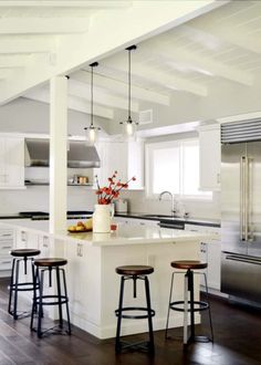 an open kitchen with white cabinets and wooden flooring, along with bar stools