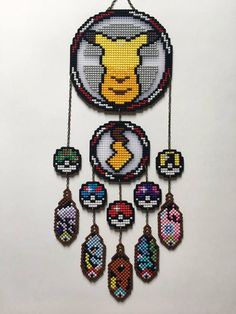 a cross stitch pokemon clock hanging from a chain on a white wall next to other items