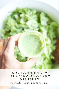 a person is holding a small cup in front of a bowl of salad with avocado dressing