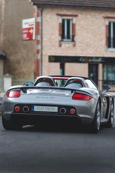 a silver sports car parked on the street in front of a building with red shutters