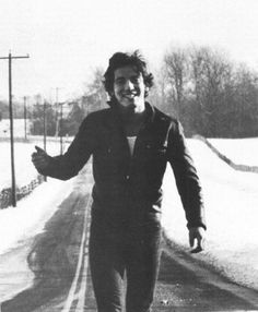 black and white photograph of a man skateboarding down a road in the middle of winter